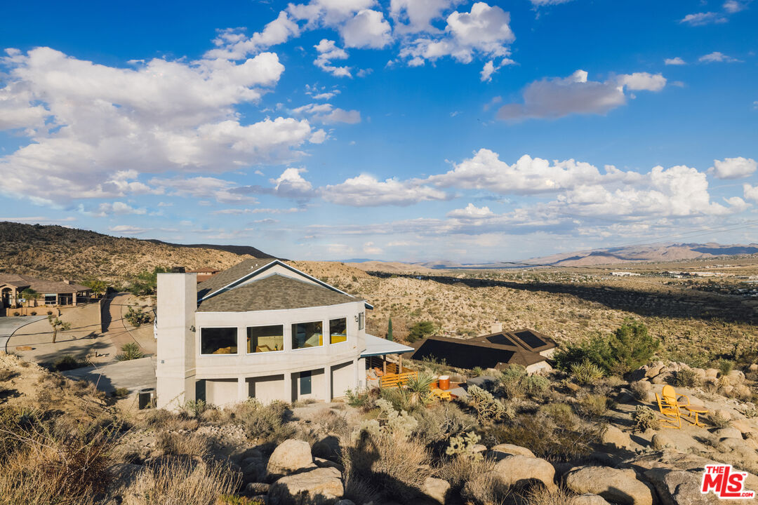 Modern desert home on a rocky hillside, with yellow outdoor chairs and distant mountain ranges.