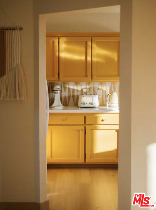 Kitchen with yellow cabinets, geometric backsplash, and white countertop appliances.
