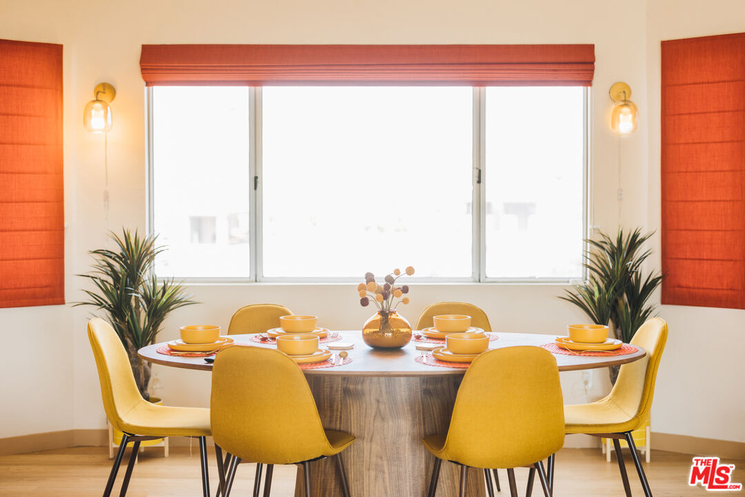 Dining room with a set round table, mustard-yellow chairs, and orange window shades.