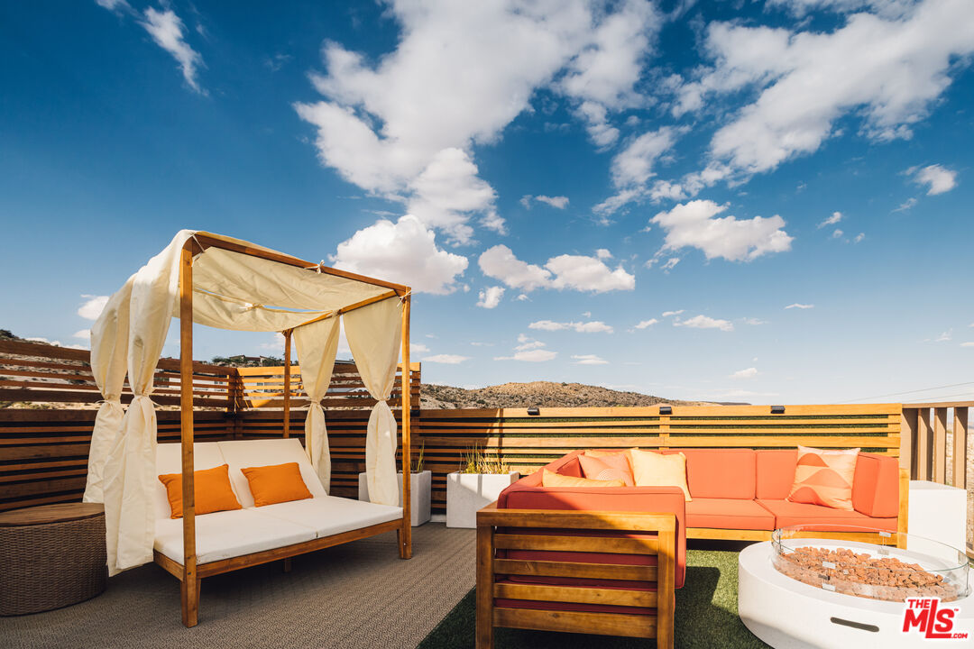 Outdoor patio with a curtained daybed, coral sectional, and fire pit overlooking desert hills.