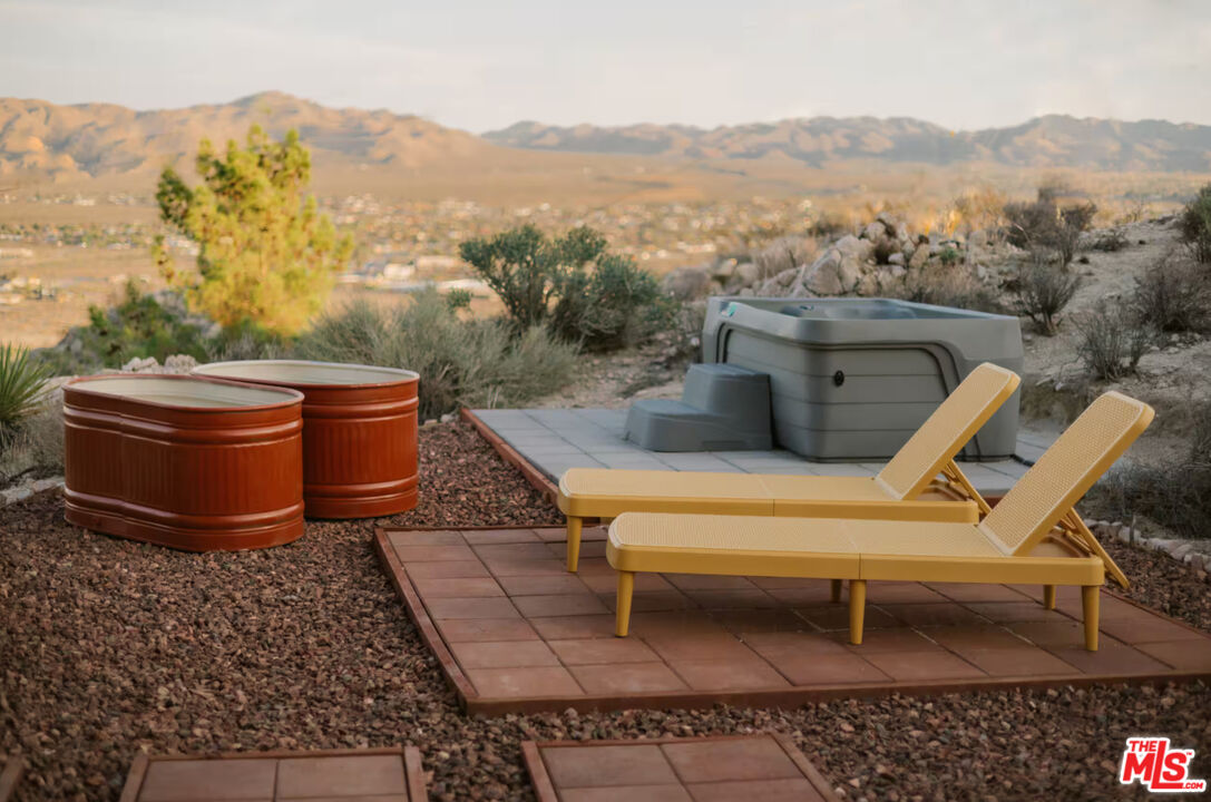 Outdoor hot tub patio with lounge chairs overlooking a rocky desert valley and mountains.