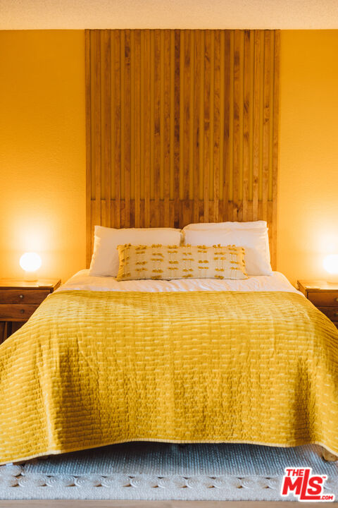Bedroom with a neatly made bed, yellow quilt, and tall wood-slat headboard.