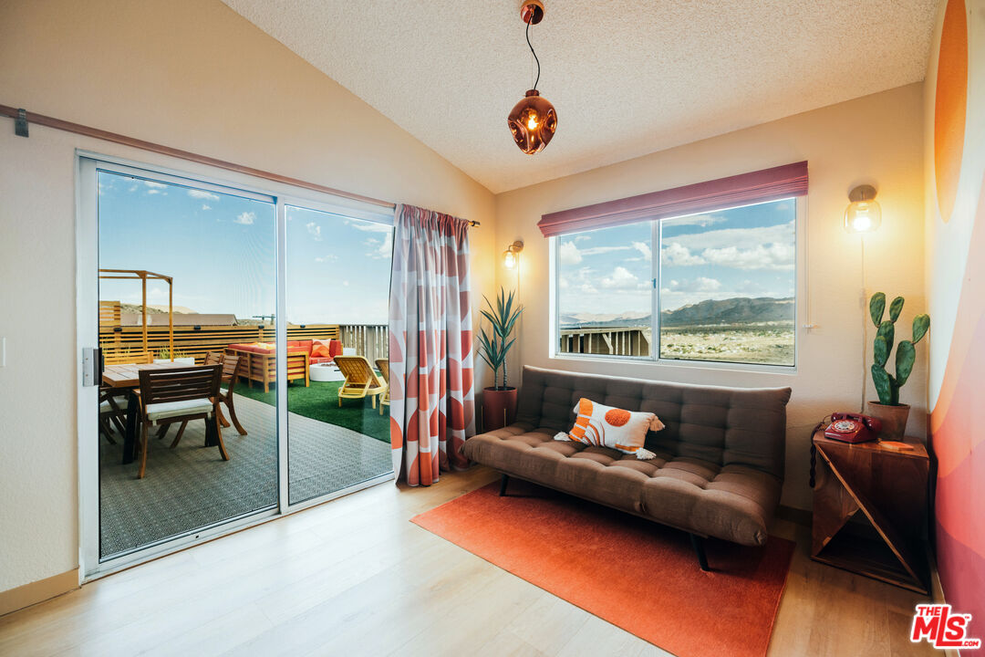 Living room with a brown sofa and orange rug, opening onto a patio with mountain views.