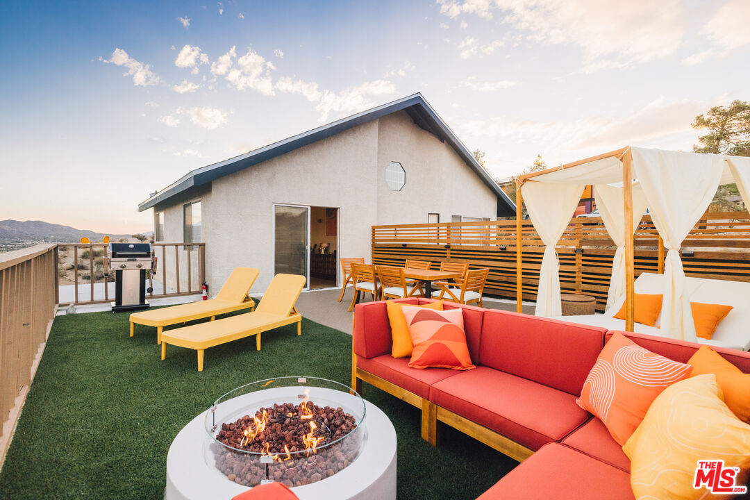 Rooftop patio with a round fire pit, colorful lounge seating, and a white fabric pergola.