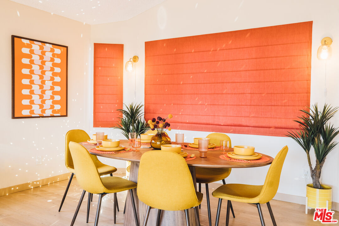 Staged dining room with a set table, mustard-yellow chairs, and large coral-orange window shades.