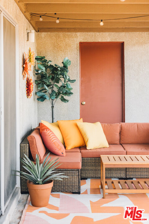 Covered patio with wicker seating, colorful cushions, potted plants, and string lights.