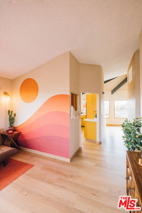 Hallway with a colorful desert-inspired mural, pale wood floors, and a view into a yellow kitchen.