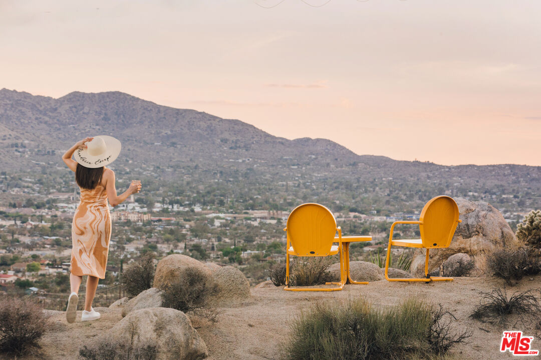 Rocky desert overlook with orange chairs facing a mountain town, while a woman takes in the view.