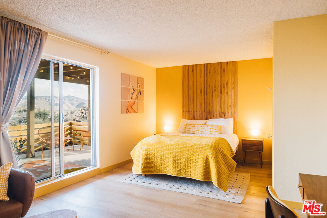 Bedroom with a yellow bedspread and wooden slat headboard, opening onto a patio with mountain views.