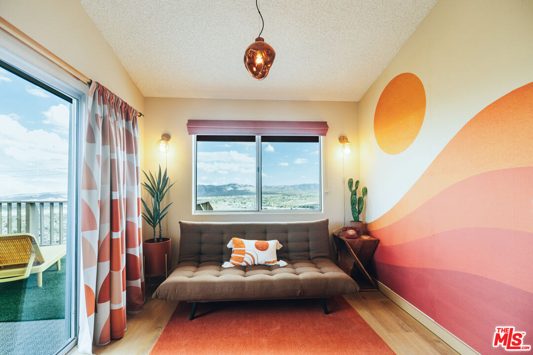 Living room with an orange mural, tufted sofa, and windows overlooking a valley and distant mountains.
