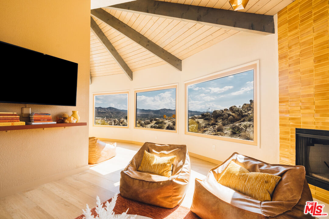 Living room with vaulted wood ceiling, lounge chairs, and large windows overlooking rocky desert mountains.