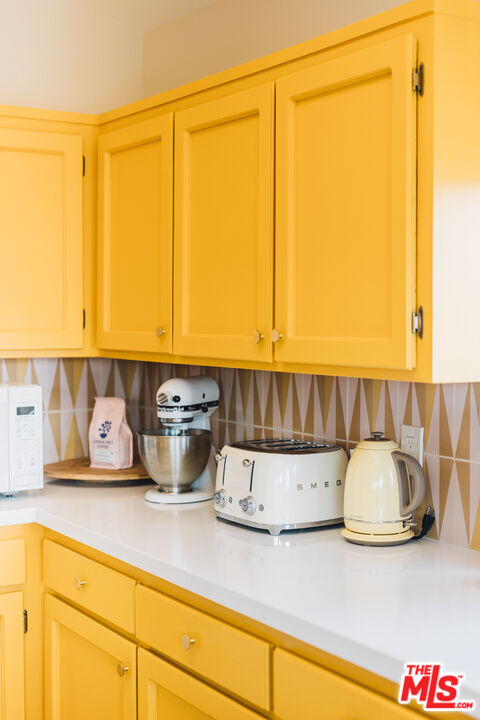 Kitchen with bright yellow cabinetry, patterned backsplash, and white countertop appliances.