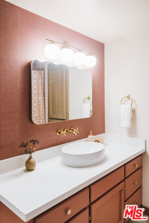 Bathroom vanity with a white vessel sink, brass fixtures, and a textured rose-colored accent wall.