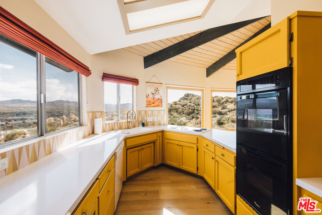Kitchen with vivid yellow cabinets and white counters, overlooking rocky desert hills through large windows.