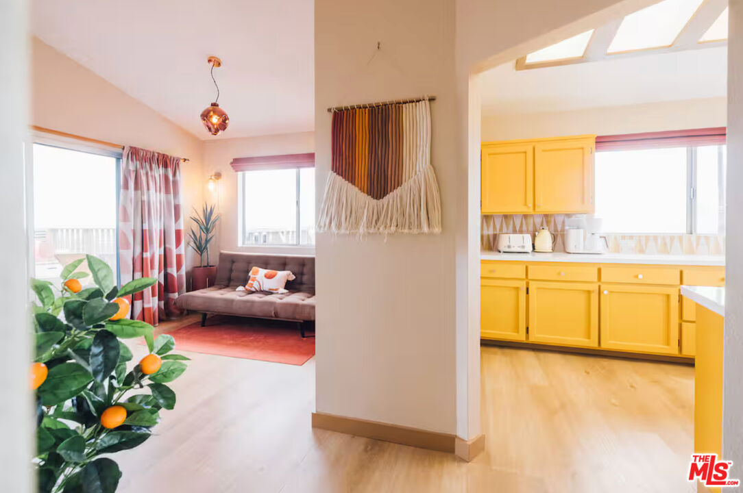 Living room opening into a bright yellow-cabinet kitchen, with a brown sofa and potted citrus tree.