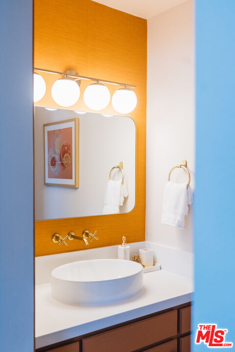 Bathroom vanity with a white vessel sink, gold faucet, and globe lights against an orange wall.