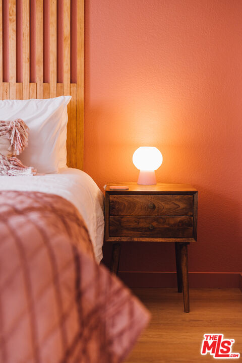 Bedroom with a wood-slat headboard, blush bedding, and glowing bedside lamp against a terracotta wall.