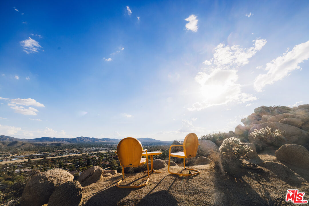 Two orange chairs overlook a desert town and distant mountains from a rocky hillside.