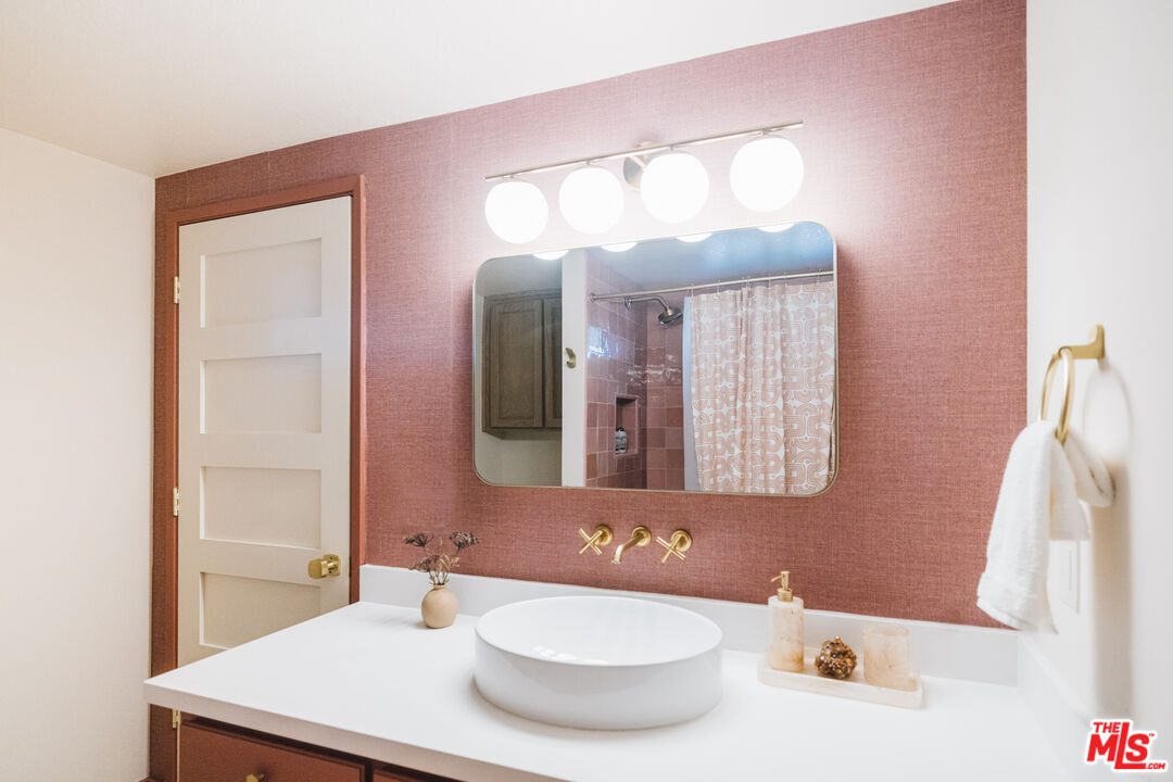 Bathroom with a white vessel sink, gold fixtures, and a muted pink accent wall.