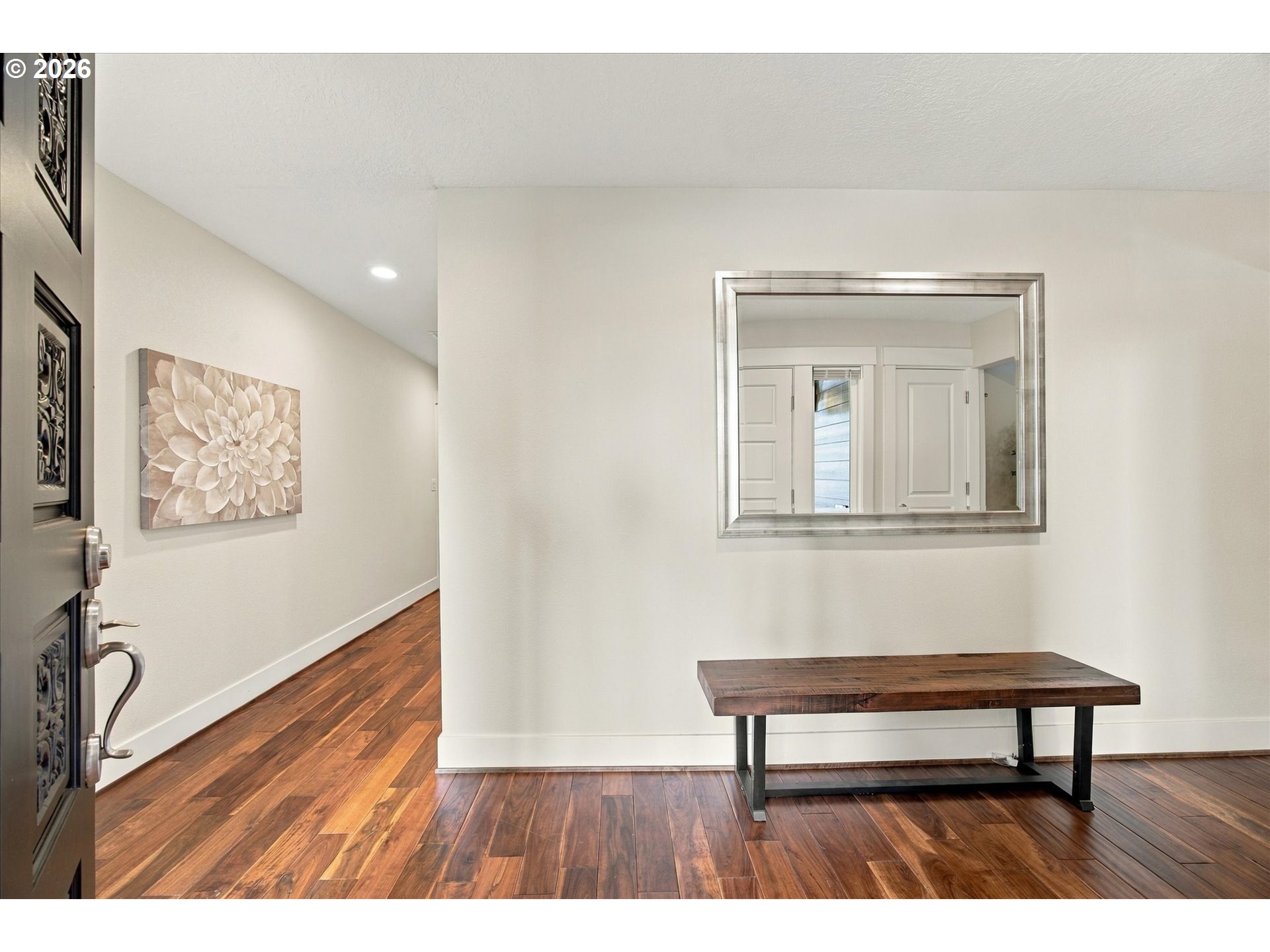 Entry hall with warm wood floors, a wooden bench, and a large wall mirror.