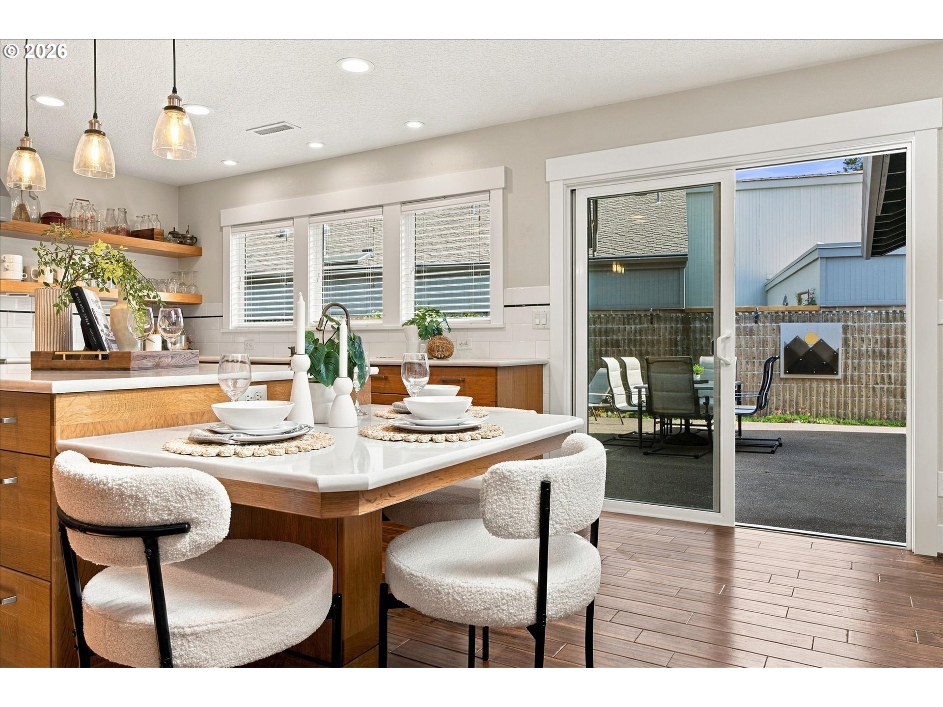 Kitchen island with white upholstered chairs and sliding doors opening to a fenced patio.