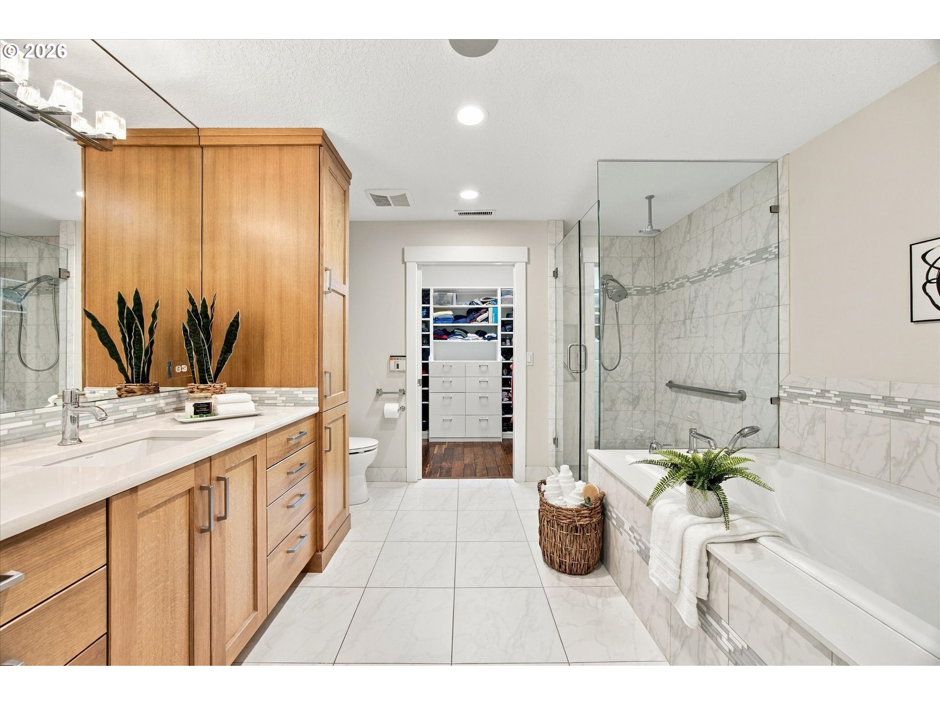 Bathroom with a wood vanity, glass shower, and bathtub beside an open dressing closet.