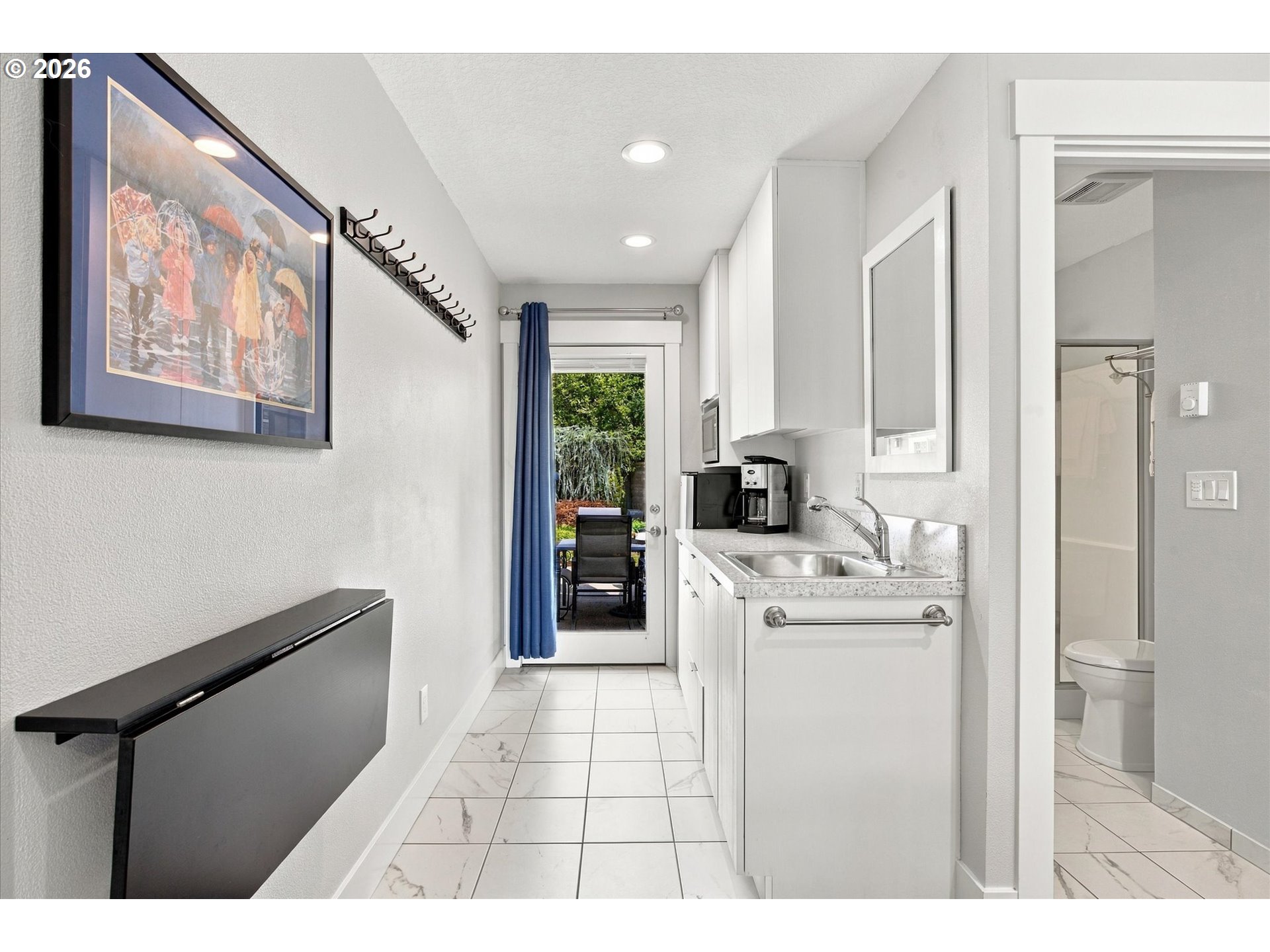Utility room with white cabinets and sink, tiled floor, and a glass door opening to a patio.