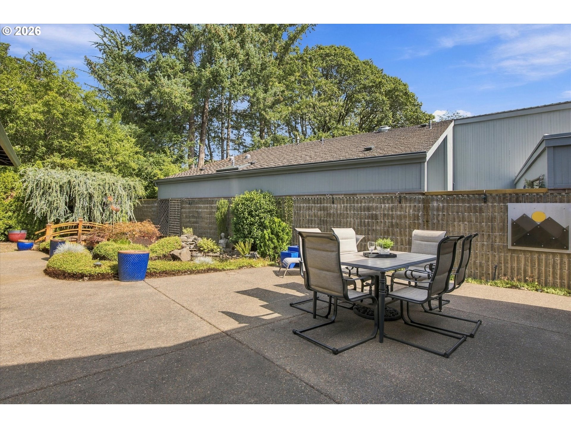 Fenced backyard patio with an outdoor dining set and landscaped garden beds.