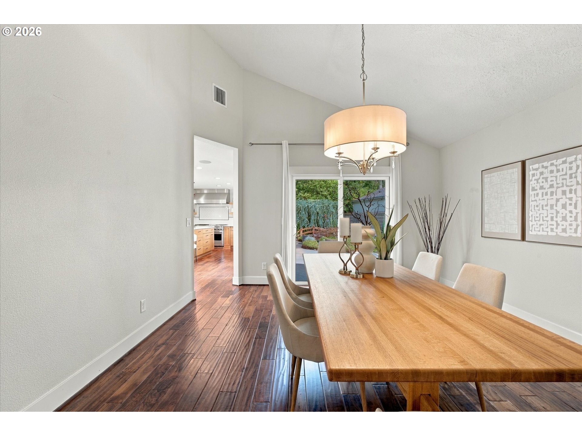 Dining room with a long wooden table and chandelier beside a sliding glass door to the garden.
