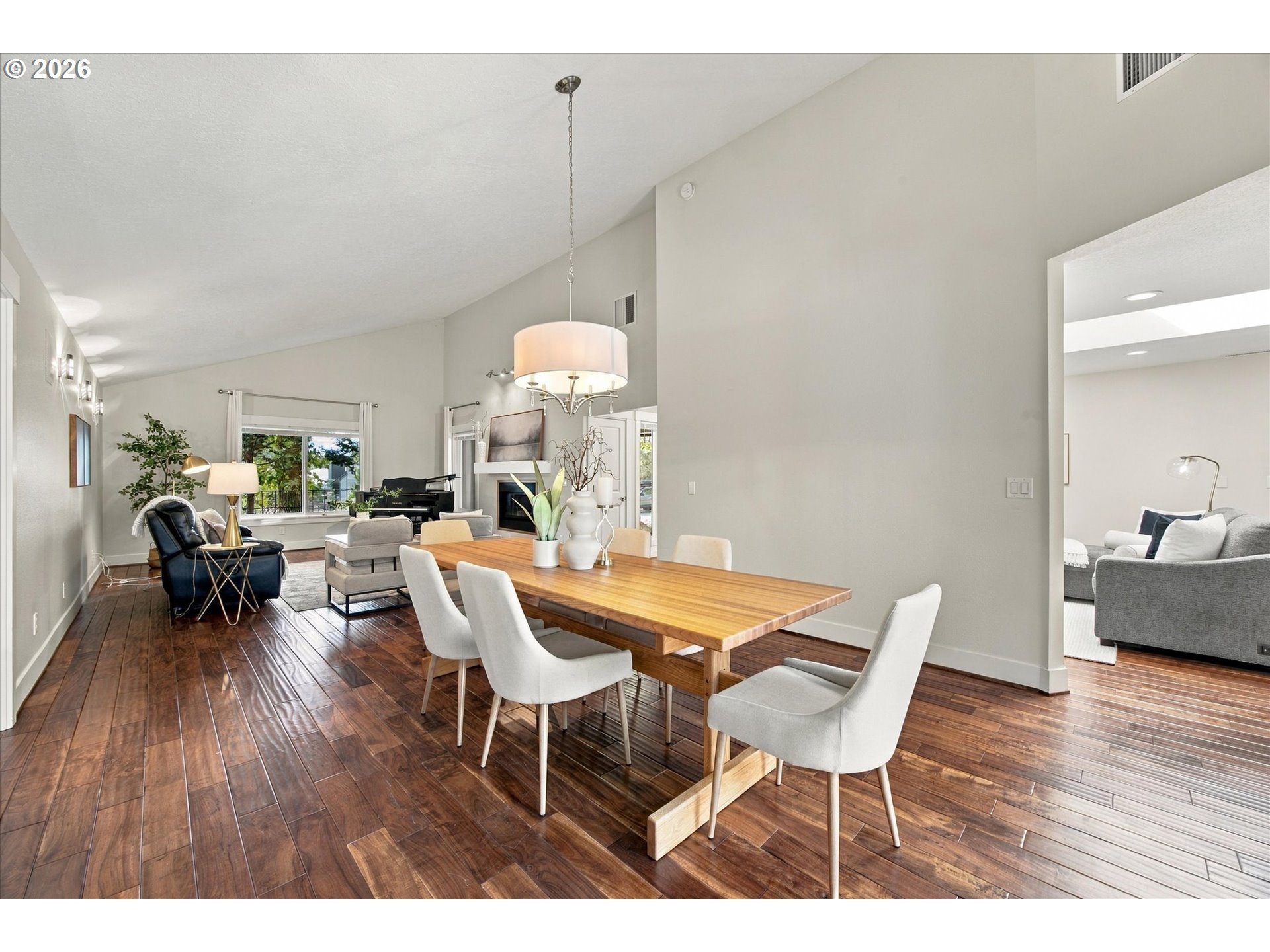Dining area with a long wooden table, white chairs, dark wood floors, and an adjoining living room.
