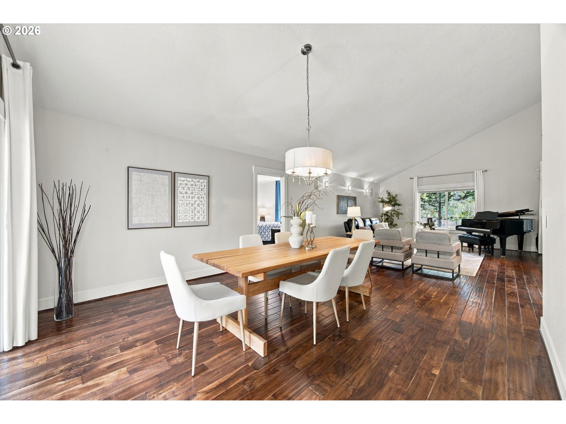 Open-plan dining and living room with a long wood table, dark hardwood floors, and a grand piano.