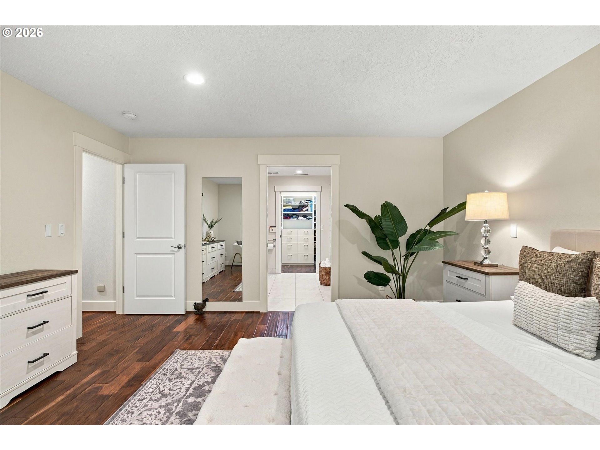 Bedroom with a large white bed, dark wood floors, and open views into the bathroom and walk-in closet.