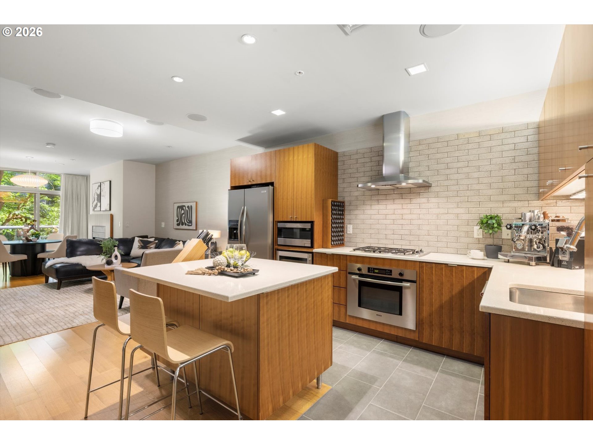 Modern kitchen with a large white island, warm wood cabinetry, and pale brick backsplash.