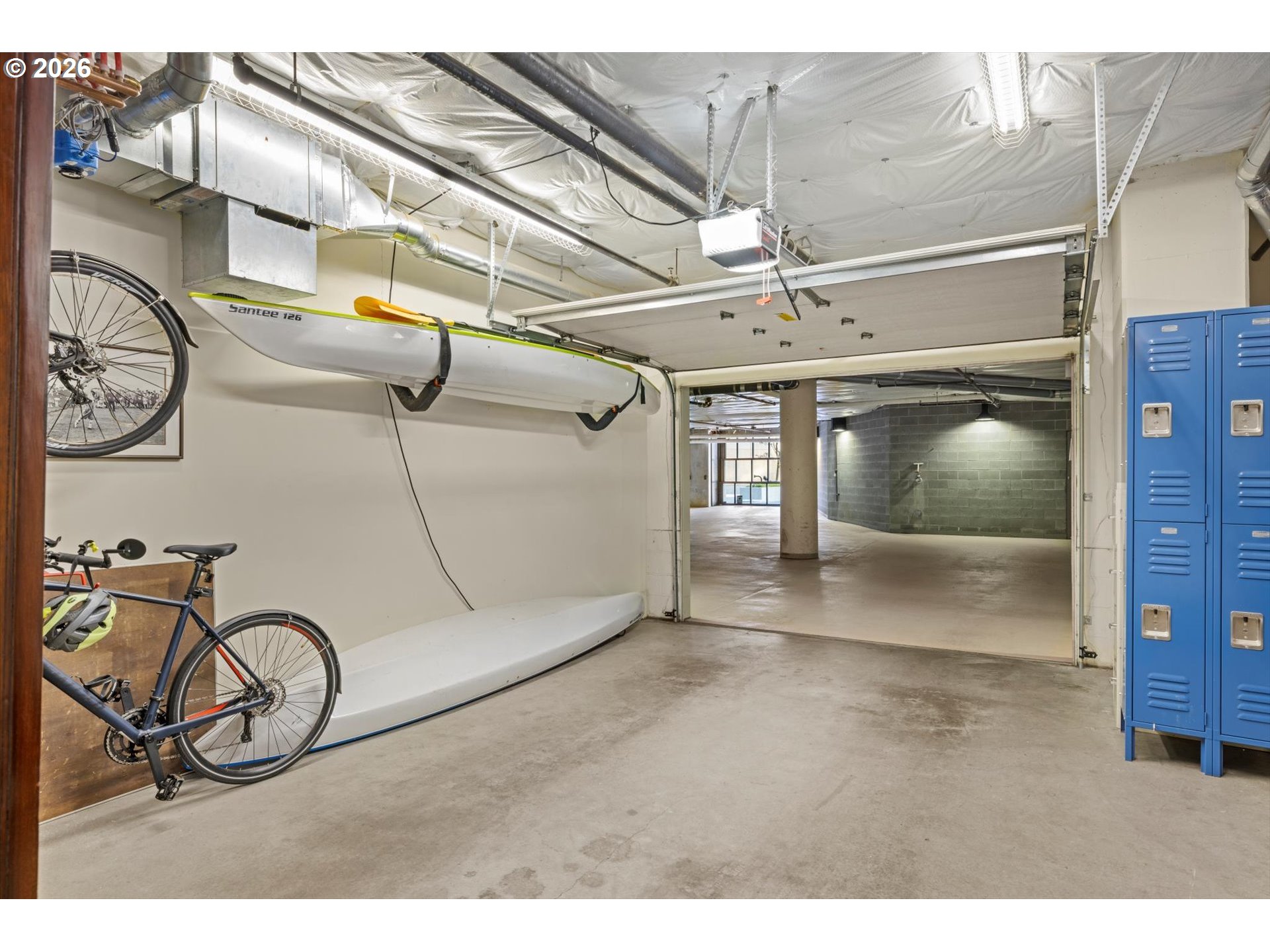 Garage storage area with blue lockers, bicycles, and kayaks mounted on the wall.
