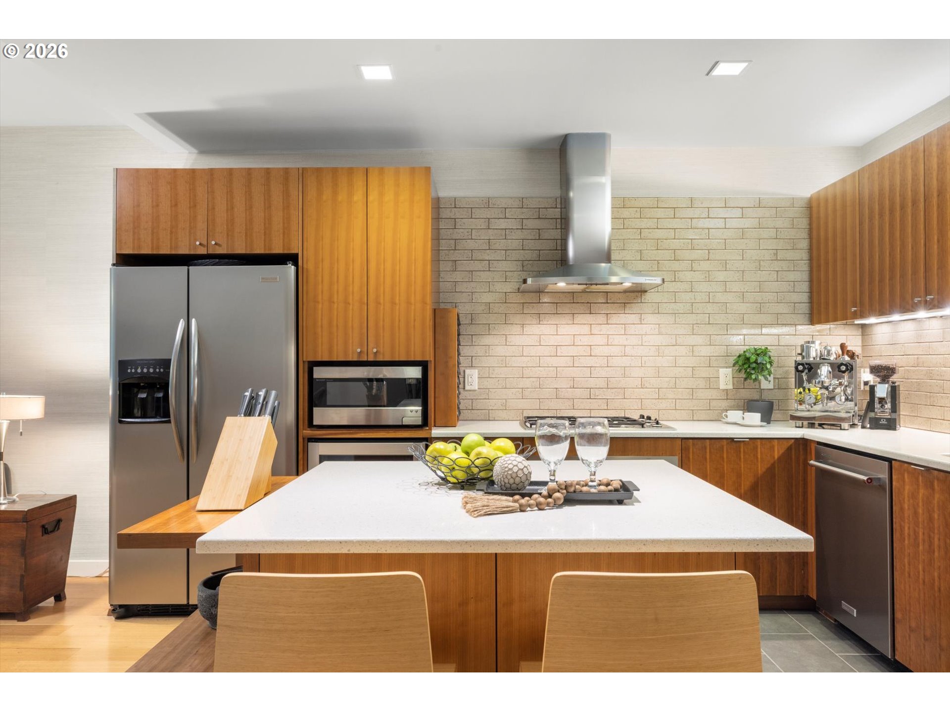 Modern kitchen with warm wood cabinetry, a white island, and stainless steel appliances.