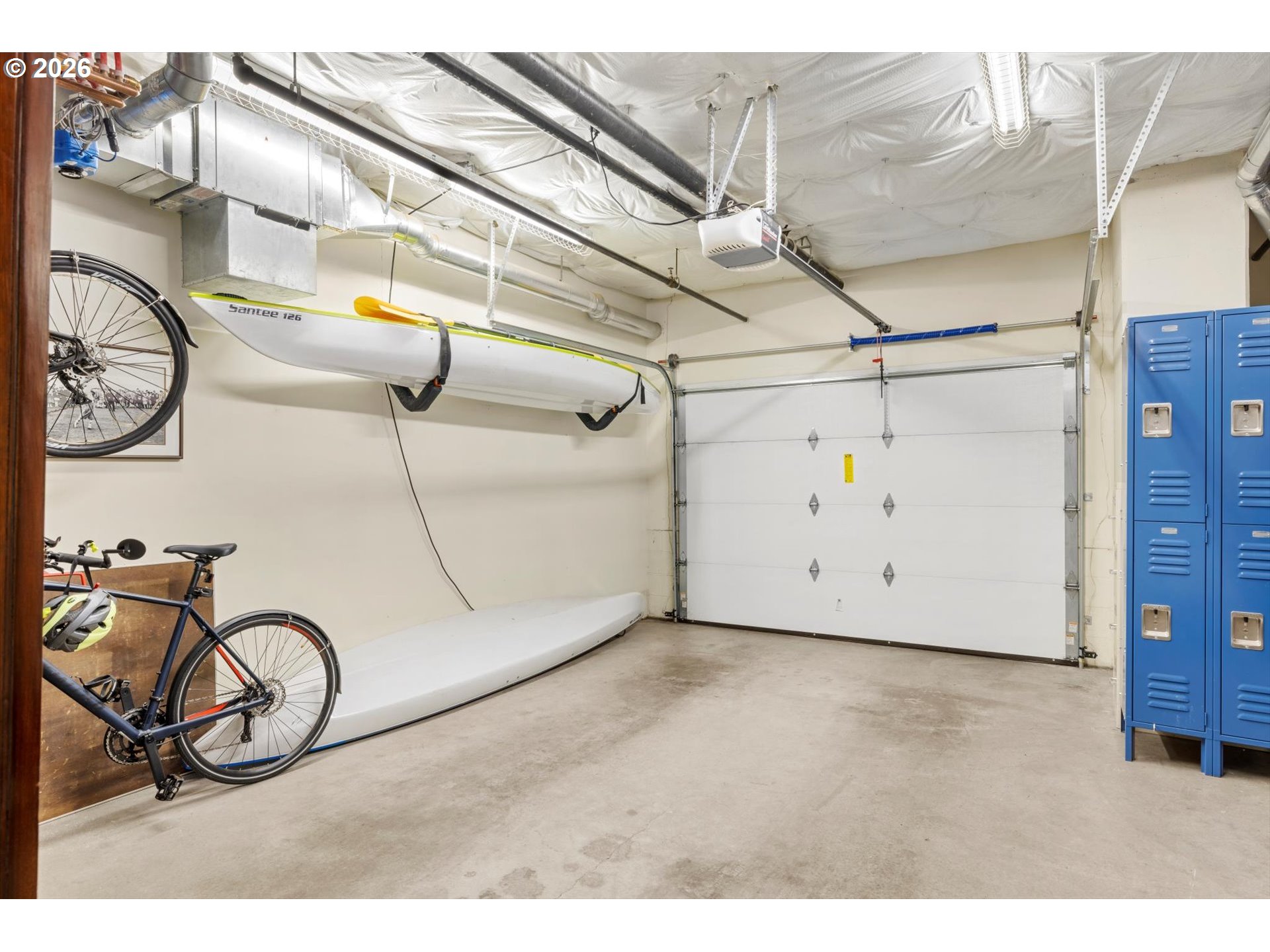 Garage with overhead kayak storage, bicycles, blue lockers, and a large sectional garage door.