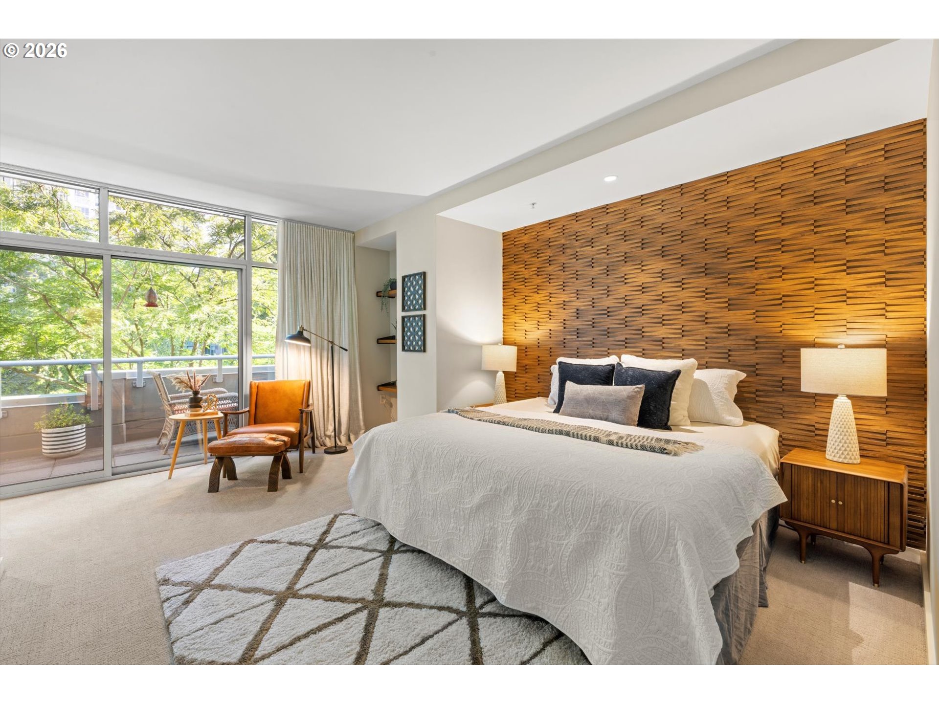 Staged bedroom with a sculptural wood accent wall and sliding doors to a leafy balcony.