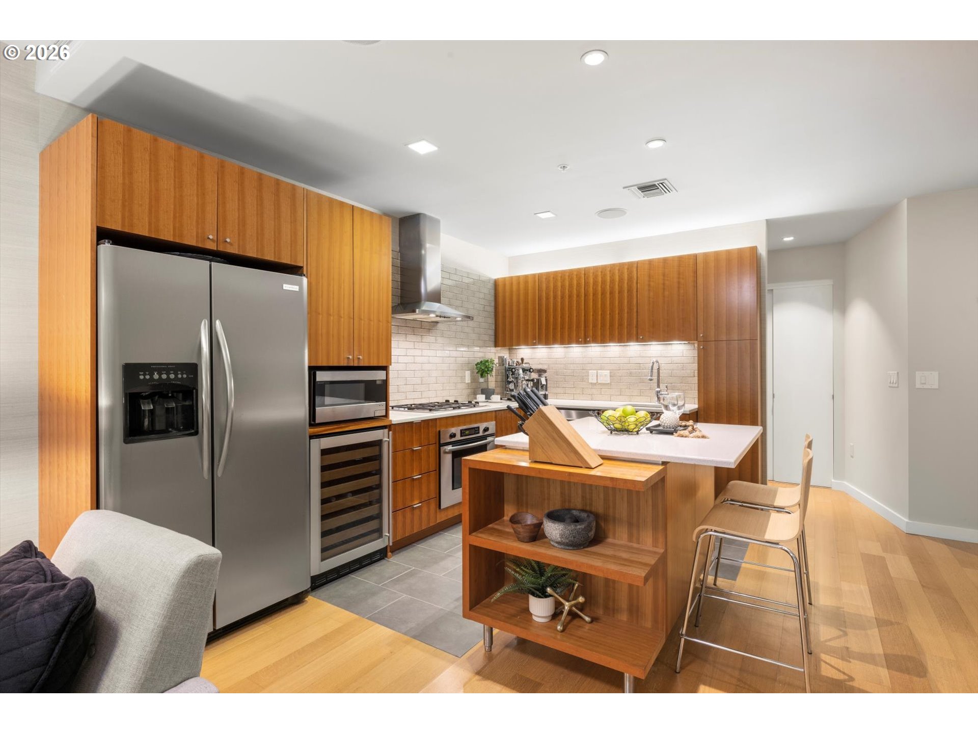 Modern kitchen with warm wood cabinetry, stainless steel appliances, and a white island with seating.