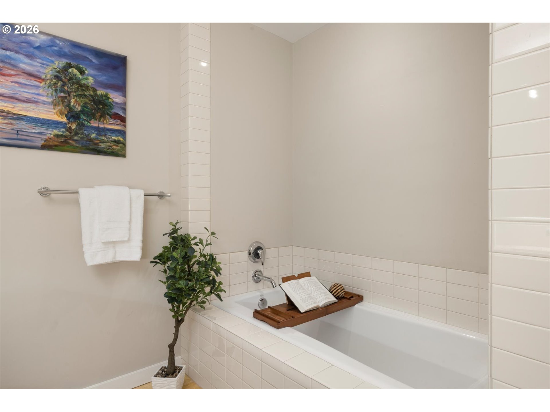 Bathroom with a white tiled bathtub, chrome fixtures, and a wooden tray holding an open book.
