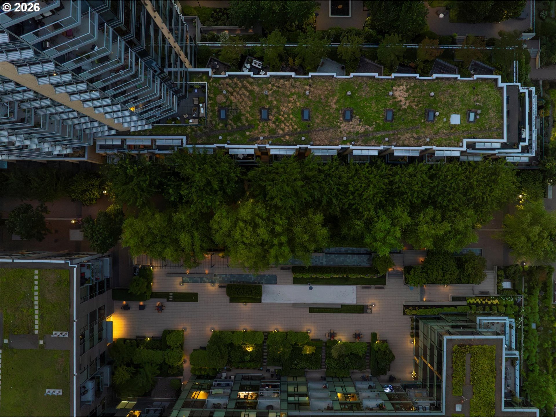 Aerial view of a landscaped rooftop courtyard with a long green roof and illuminated garden paths.