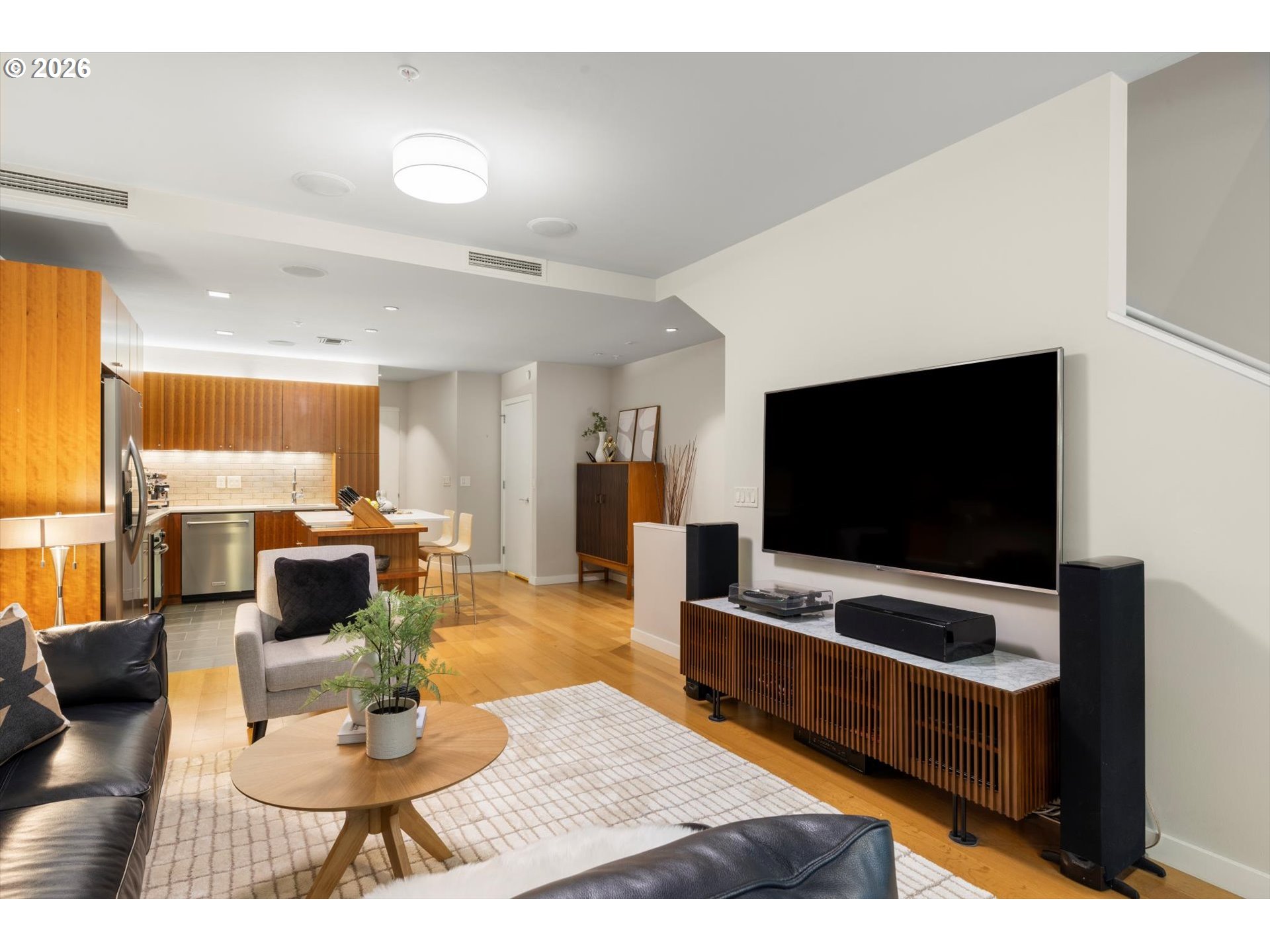 Open-plan living room and kitchen with wood cabinetry, hardwood floors, and a wall-mounted television.