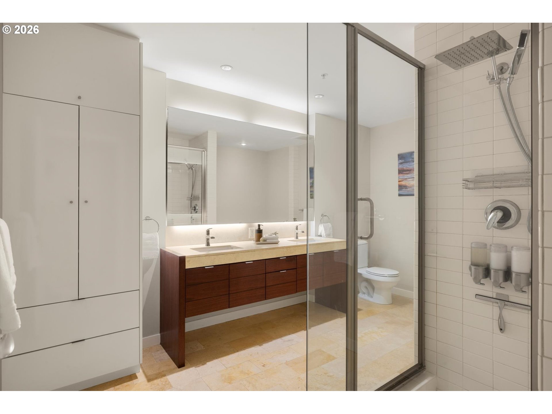 Modern bathroom with a glass shower, dark wood vanity, large mirror, and built-in cabinetry.