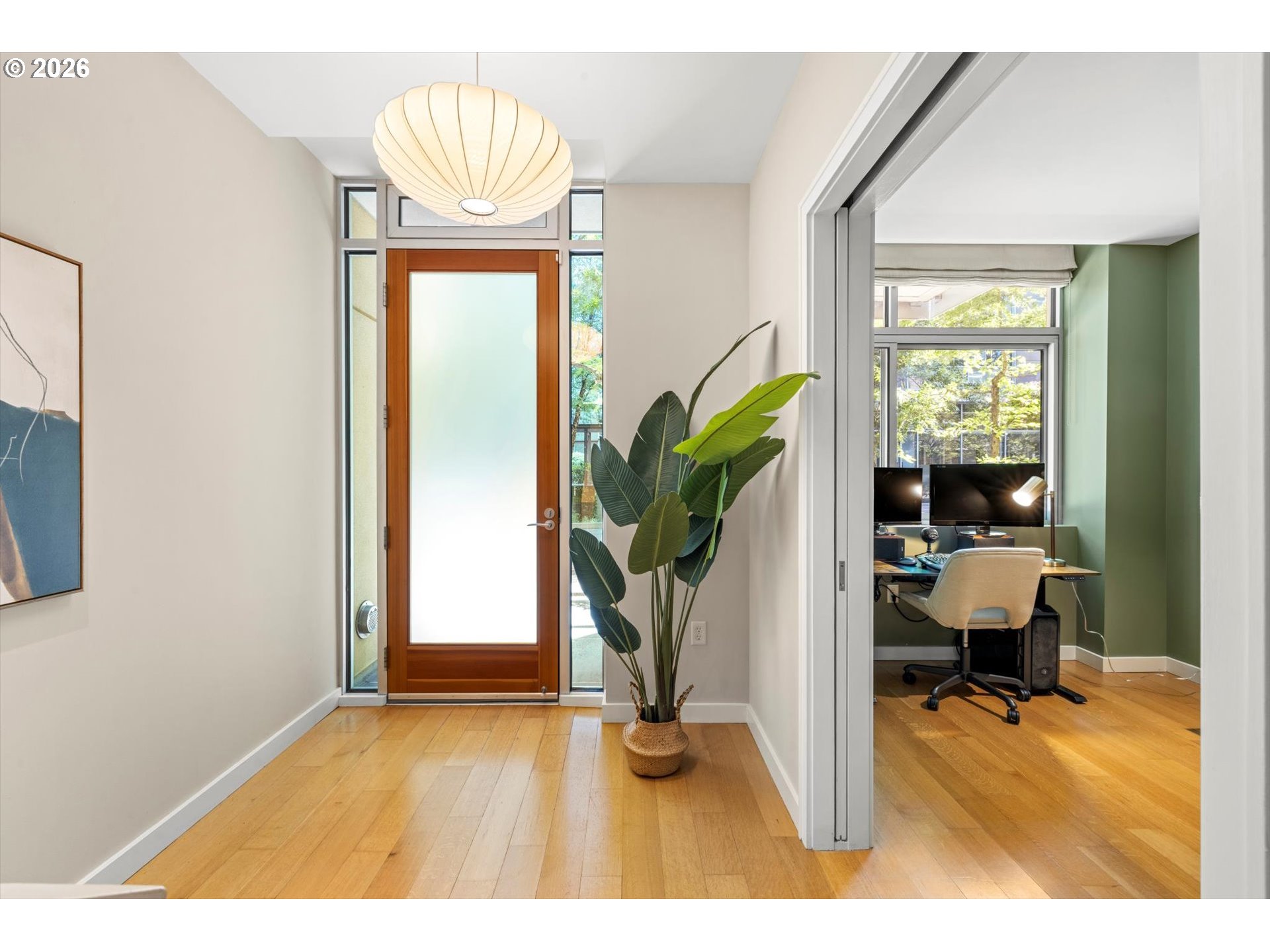 Entry hall with a frosted-glass wood door, hardwood floors, pendant light, and a view into a green-walled office.