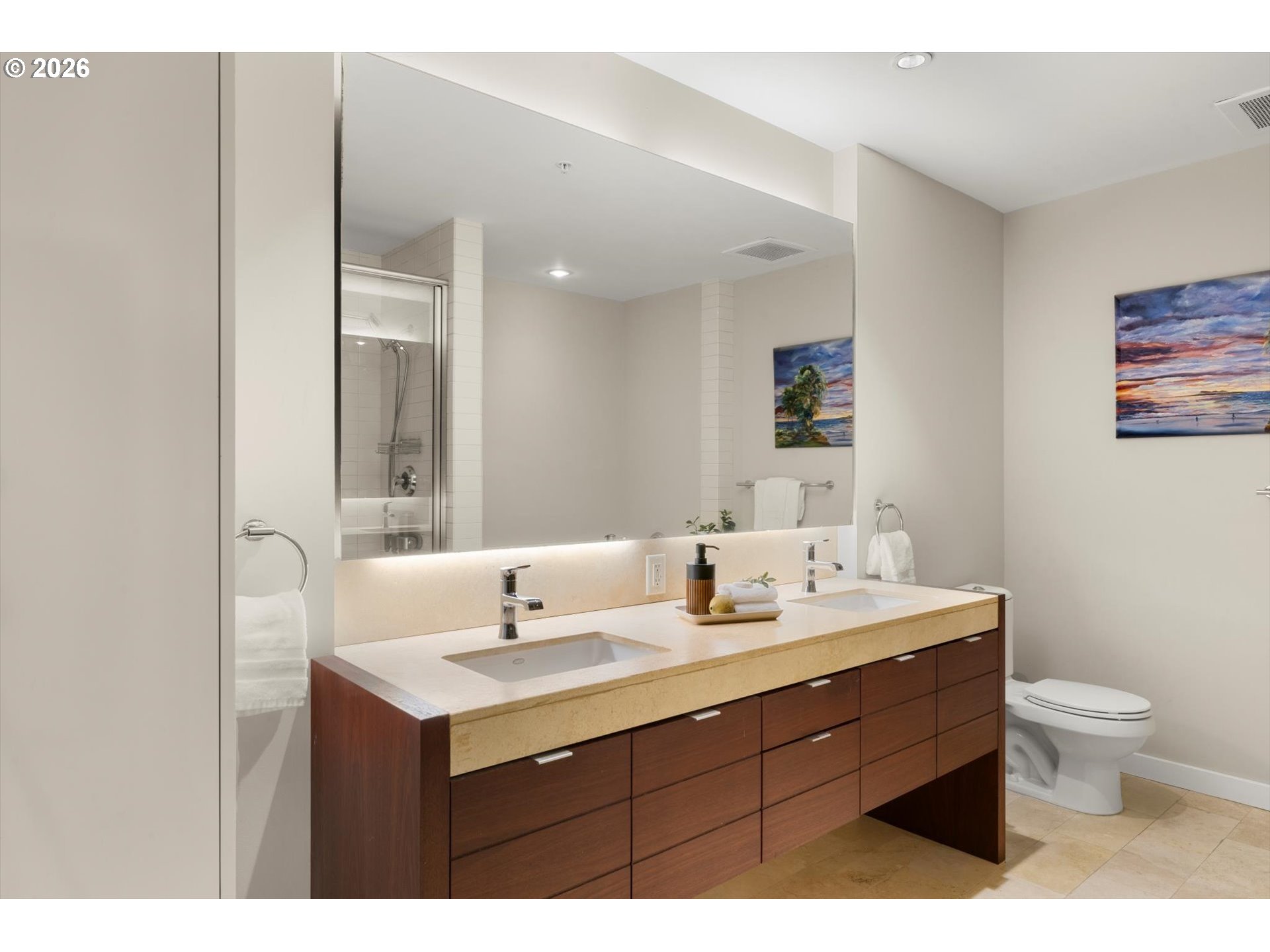 Modern bathroom with a long double-sink vanity, dark wood drawers, and glass-enclosed shower.