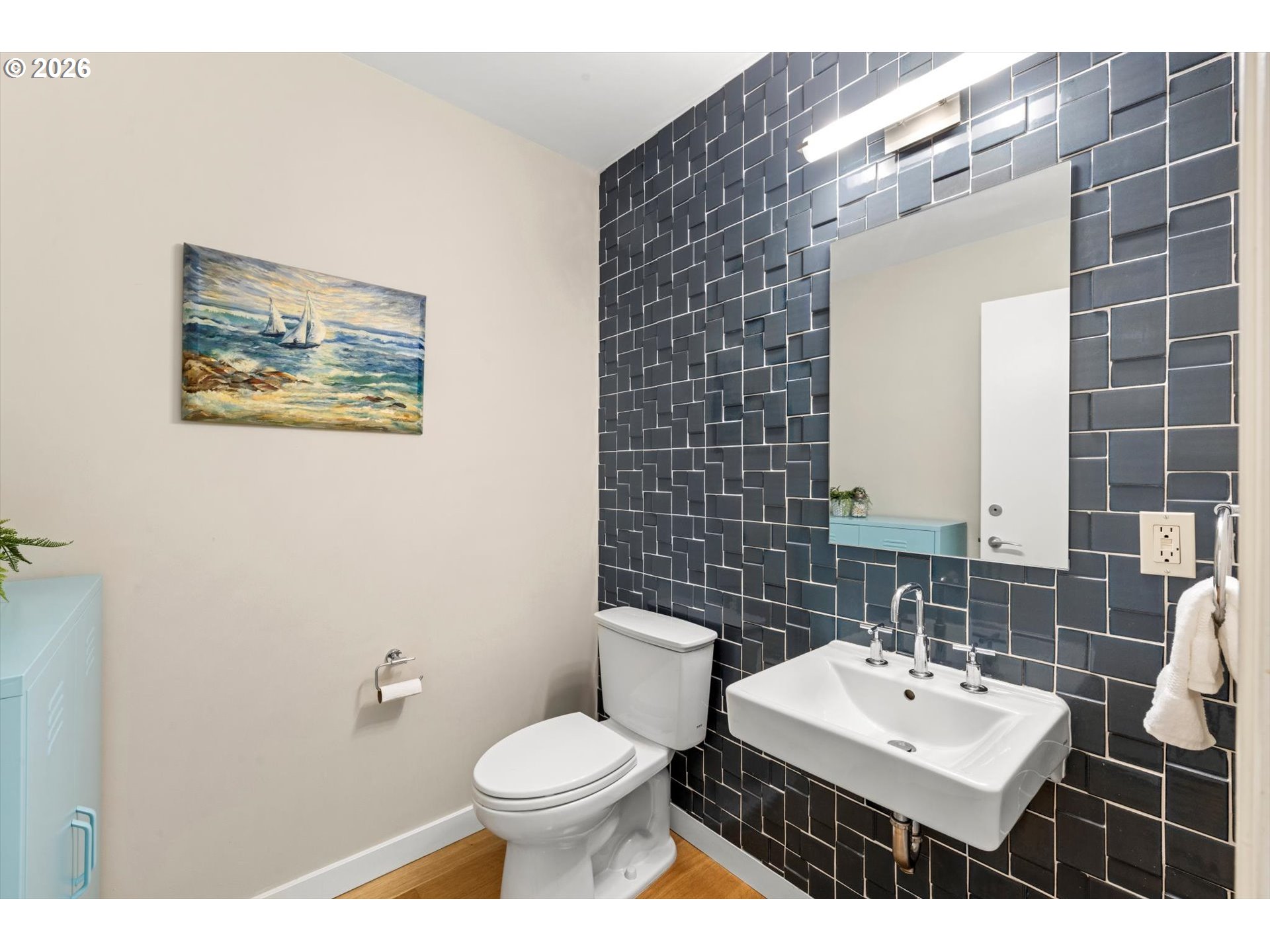 Bathroom with dark geometric tile, a white wall-mounted sink, and sailboat artwork.