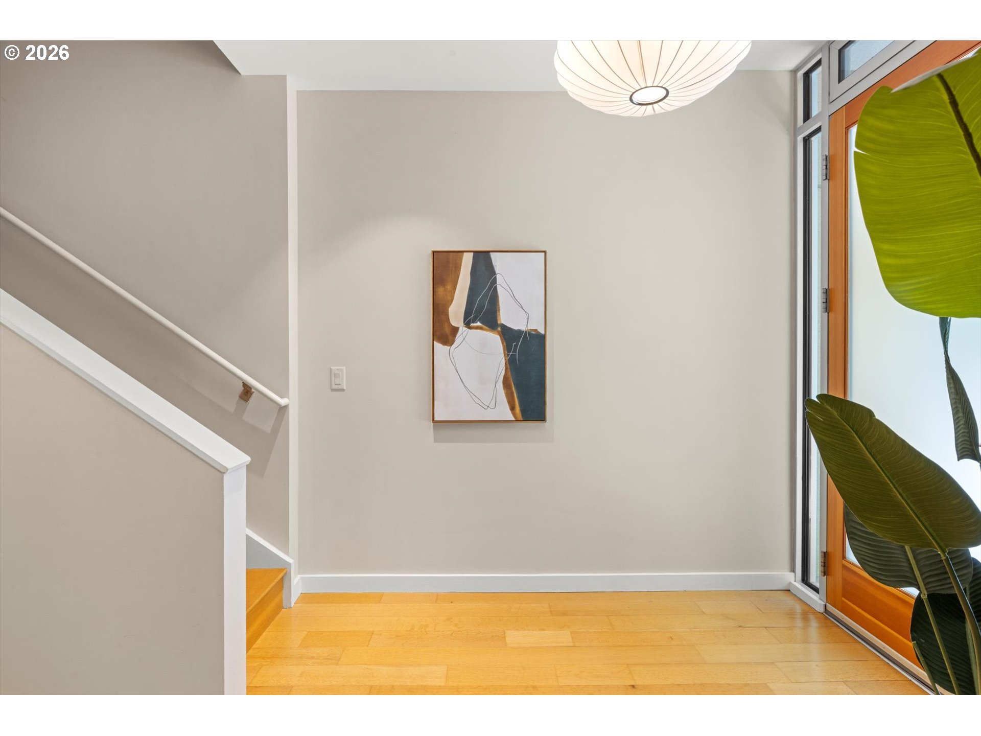 Entry foyer with wood floors, a staircase, abstract art, and a glass door beside a leafy plant.