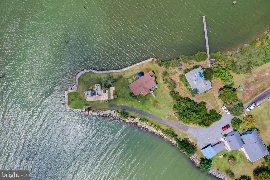 Aerial view of a waterfront home on a grassy peninsula with a rocky shoreline and long pier.