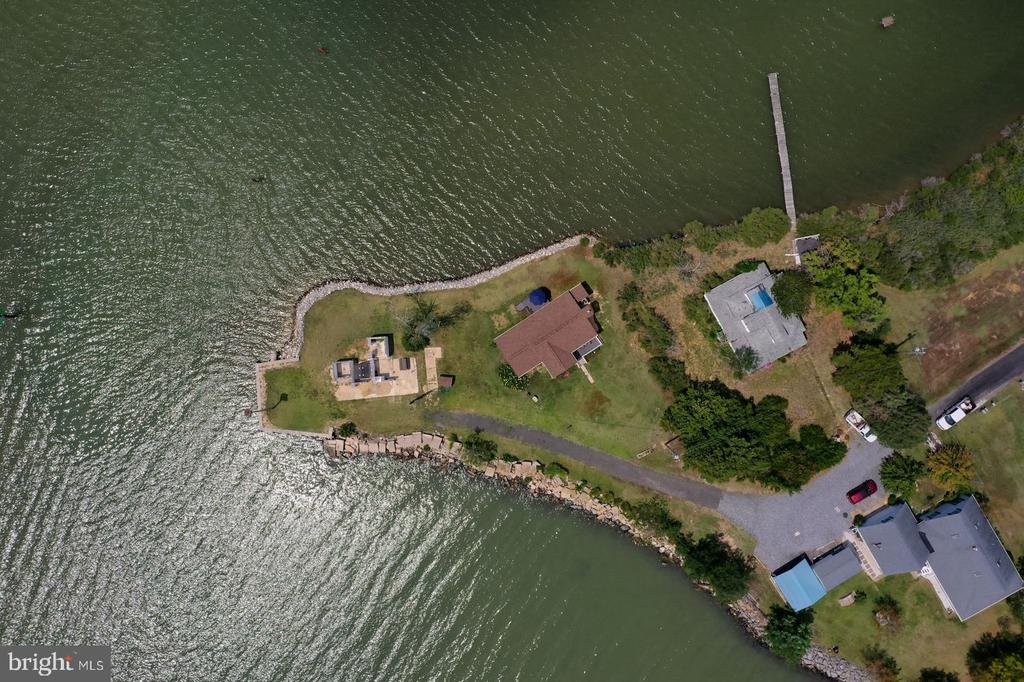 Waterfront home on a narrow peninsula, with a long dock and rock-lined shoreline.