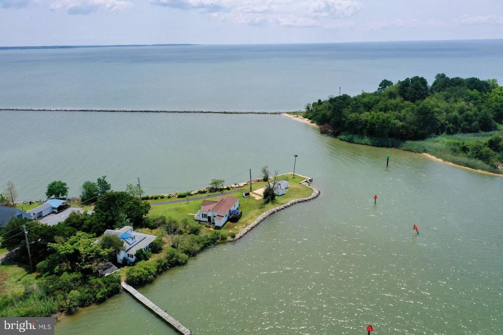 Waterfront home on a green peninsula, with a dock and wooded shoreline across the inlet.