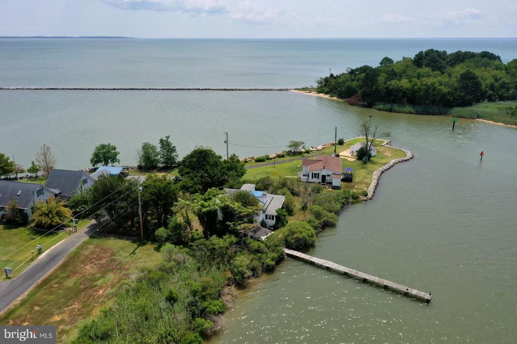 Aerial view of waterfront homes, a grassy point, and a long pier extending into the inlet.